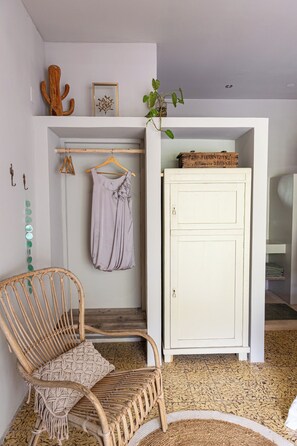 Ein Zimmer mit einem Korbstuhl, einer Kleiderstange, einem Schrank und einer Pflanze.
