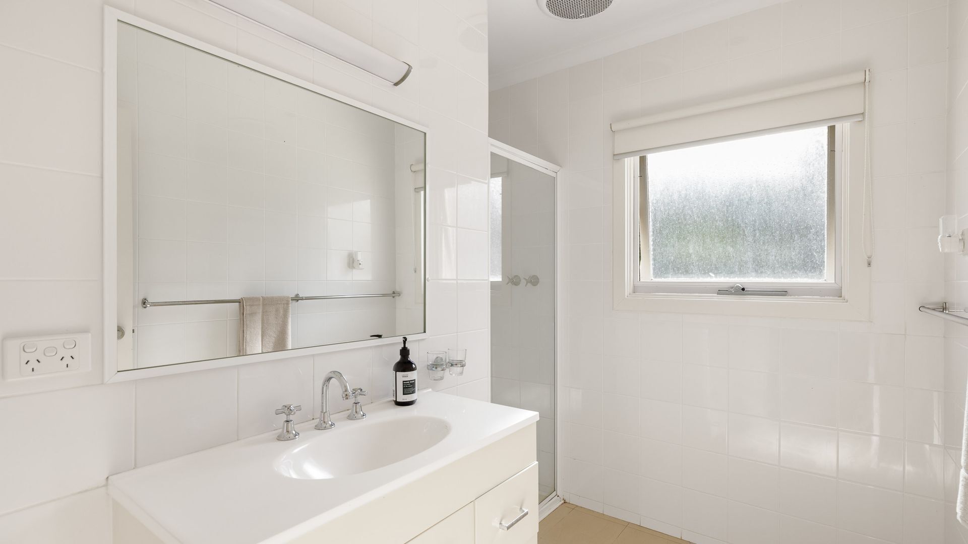 A bathroom with a white sink, mirror, and window.