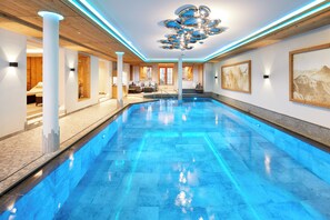 Ein großer, innenliegender Schwimmbereich mit modernem Design, umgeben von einer Lounge mit Sitzgelegenheiten und Blick ins Freie.