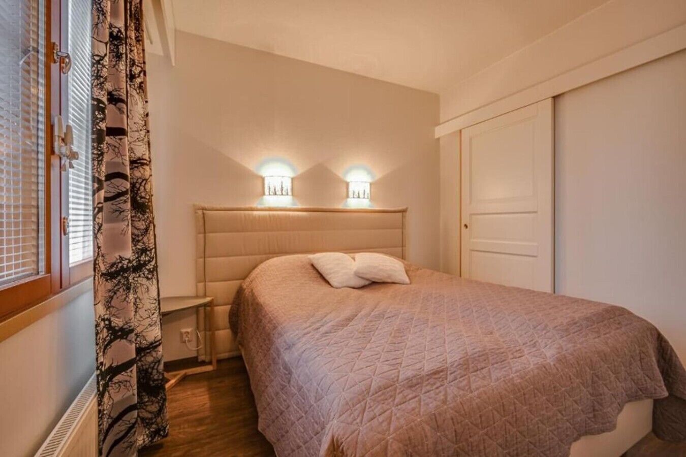 A bedroom with a bed, bedside tables, and two wall-mounted lights.