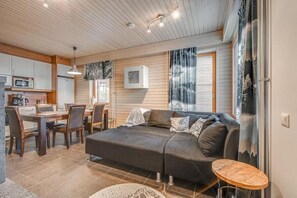 A cozy living area with a sofa, dining table, and chairs, a kitchen area with a microwave, and a large window with a view. - Länsirinne C9 | Modern 2BR Apt with Lake Views (Ruka)
