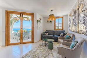 Ein Wohnzimmer mit einer Couch, Sesseln, einem Couchtisch und Meerblick durch große Glasüren.