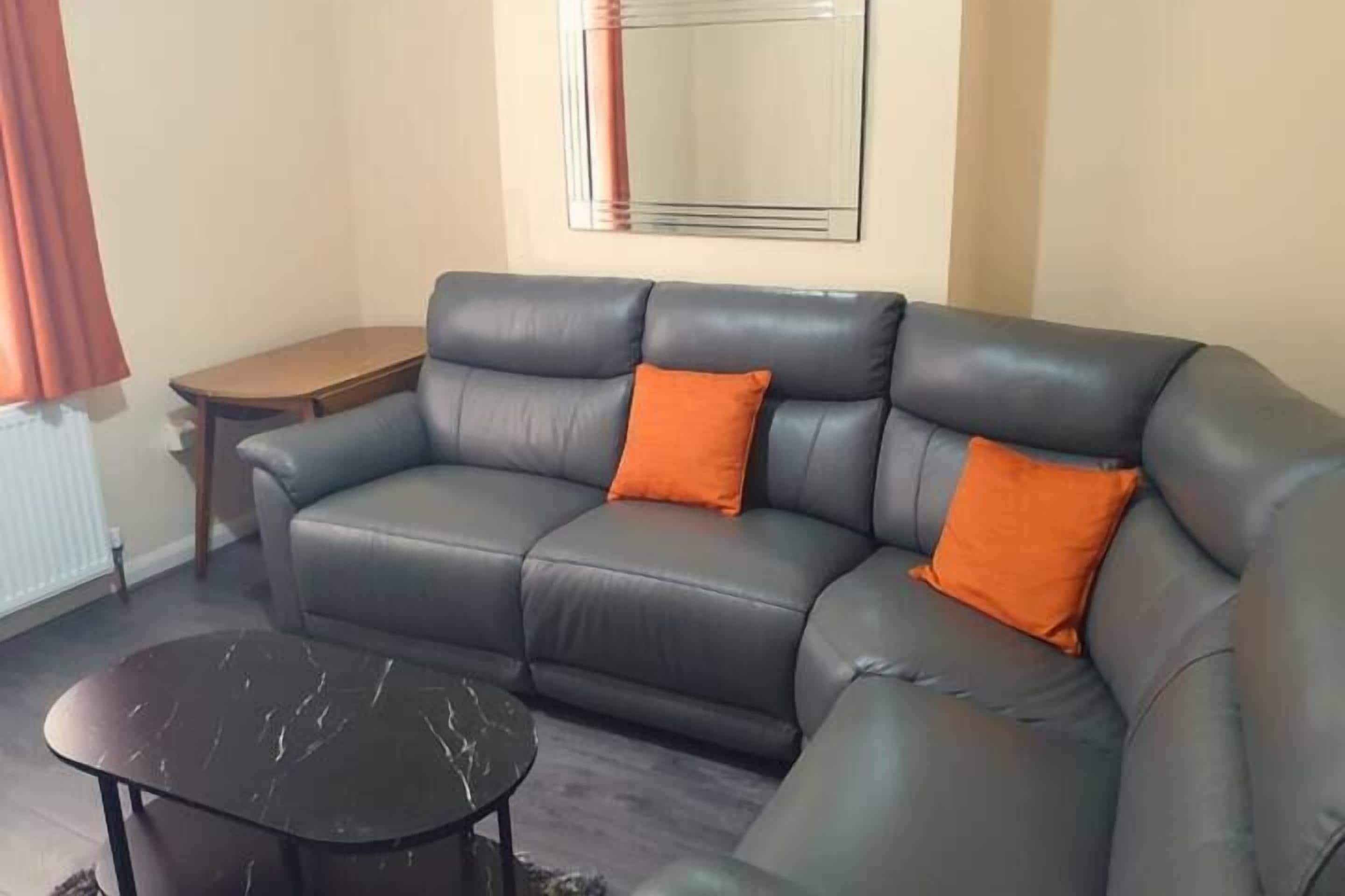 A living room with a sofa, two orange cushions, a small round table, and a mirror on the wall.