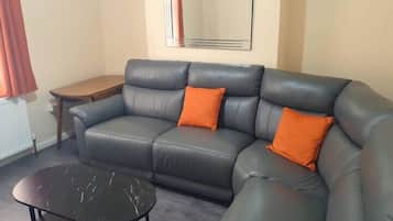 A living room with a sofa, two orange cushions, a small round table, and a mirror on the wall.