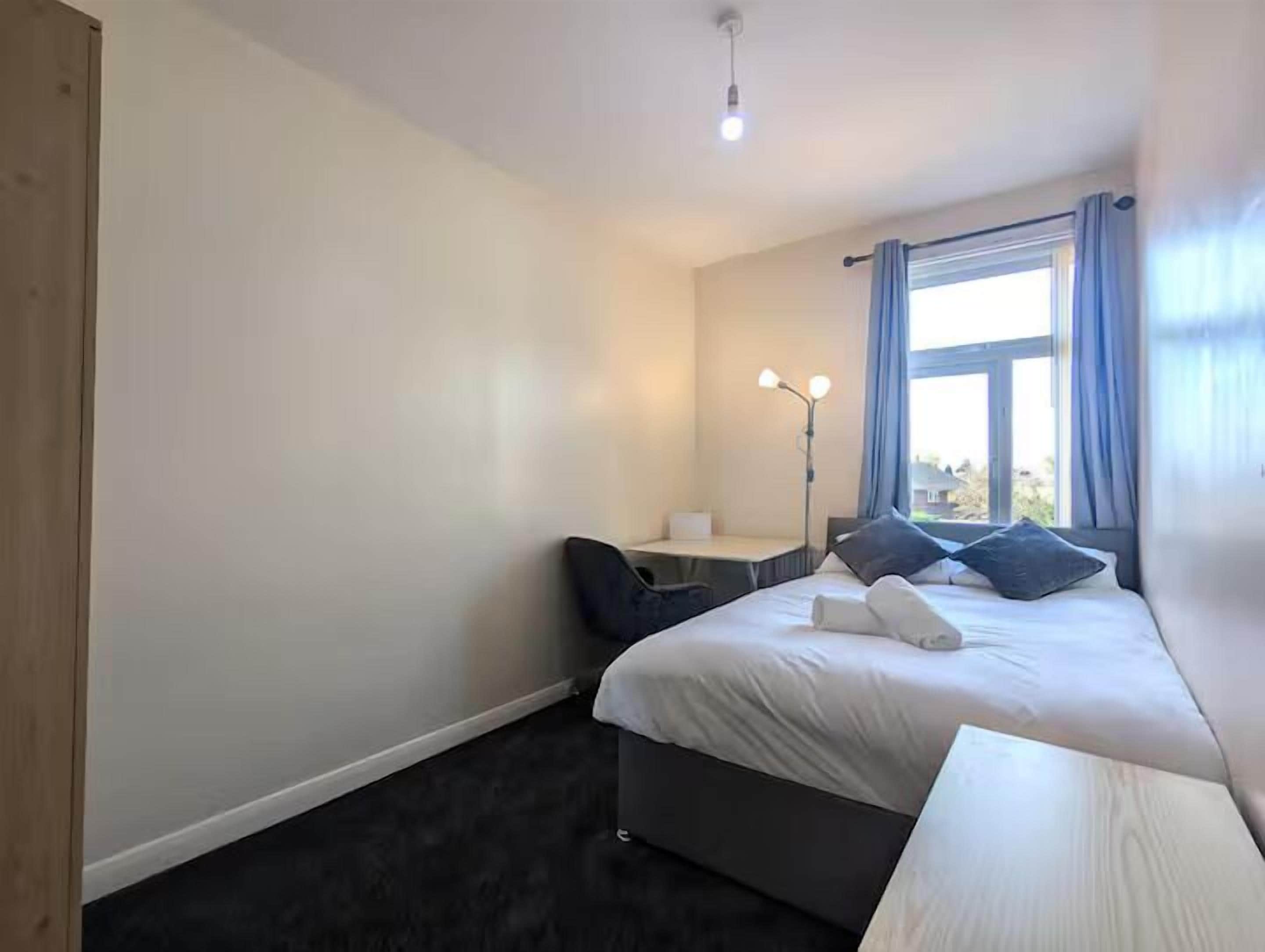 A hotel room with a bed, bedside table, lamp, and a view of the outdoors.
