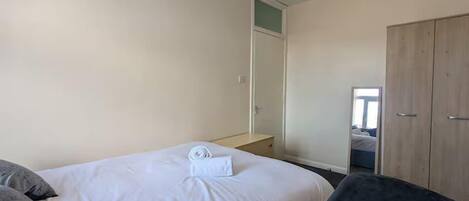 A bedroom with a bed, a chair, a wardrobe, and a mirror.