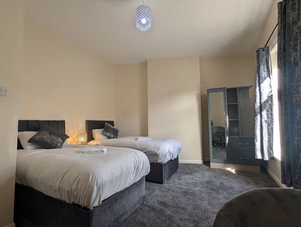 Ett hotellrum med två sängar, ett skrivbord, en stol, en garderob och en stor spegel.