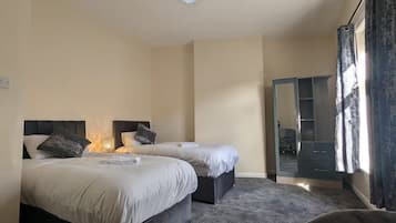 A hotel room with two beds, a desk, a chair, a wardrobe, and a large mirror.