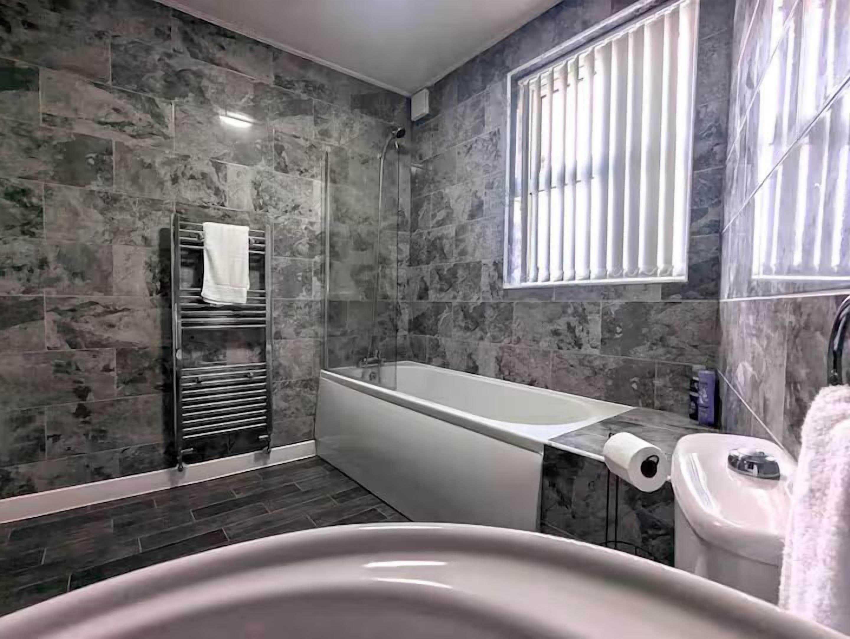 A bathroom with a bathtub, a shower, a towel rack, and a window with blinds.