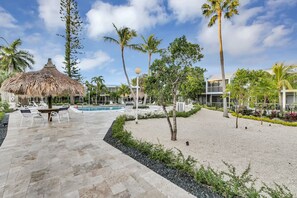 Un complexe hôtelier doté d’une piscine, de chaises longues, d’une structure à toit de chaume et de palmiers.