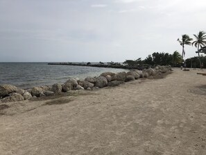 A sandy beach with a rocky breakwater and palm trees in the background. - Serene Key Largo Gem (Key Largo)
