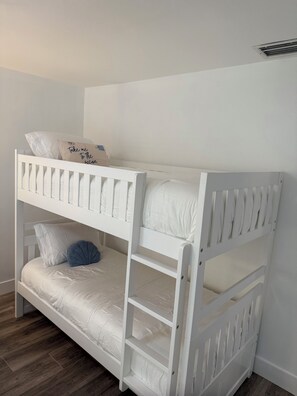 A bunk bed with a pillow that has text on it, a white wall, and a wooden floor. - Serene Key Largo Gem (Key Largo)