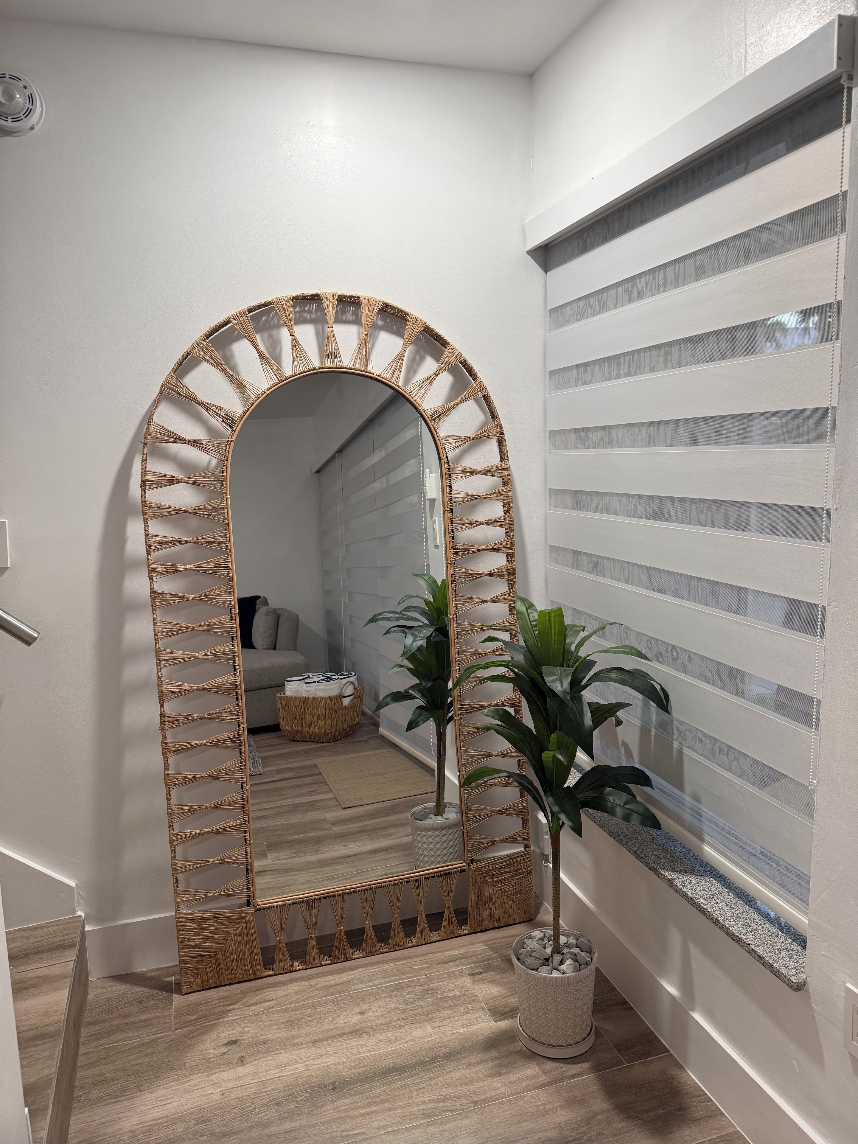 A hallway with a large mirror, a potted plant, and a window with blinds.