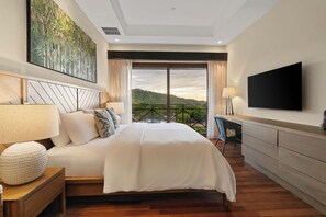 A modern bedroom with a large bed, a flat-screen TV, and a view of a mountainous landscape. - Hermosa del Mar 1-6B | Pools & Gym, Walk to Beach (Playa Hermosa)