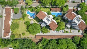 Vue aérienne d’un quartier résidentiel avec une piscine, plusieurs maisons aux toits en tuiles et une végétation luxuriante tout autour.