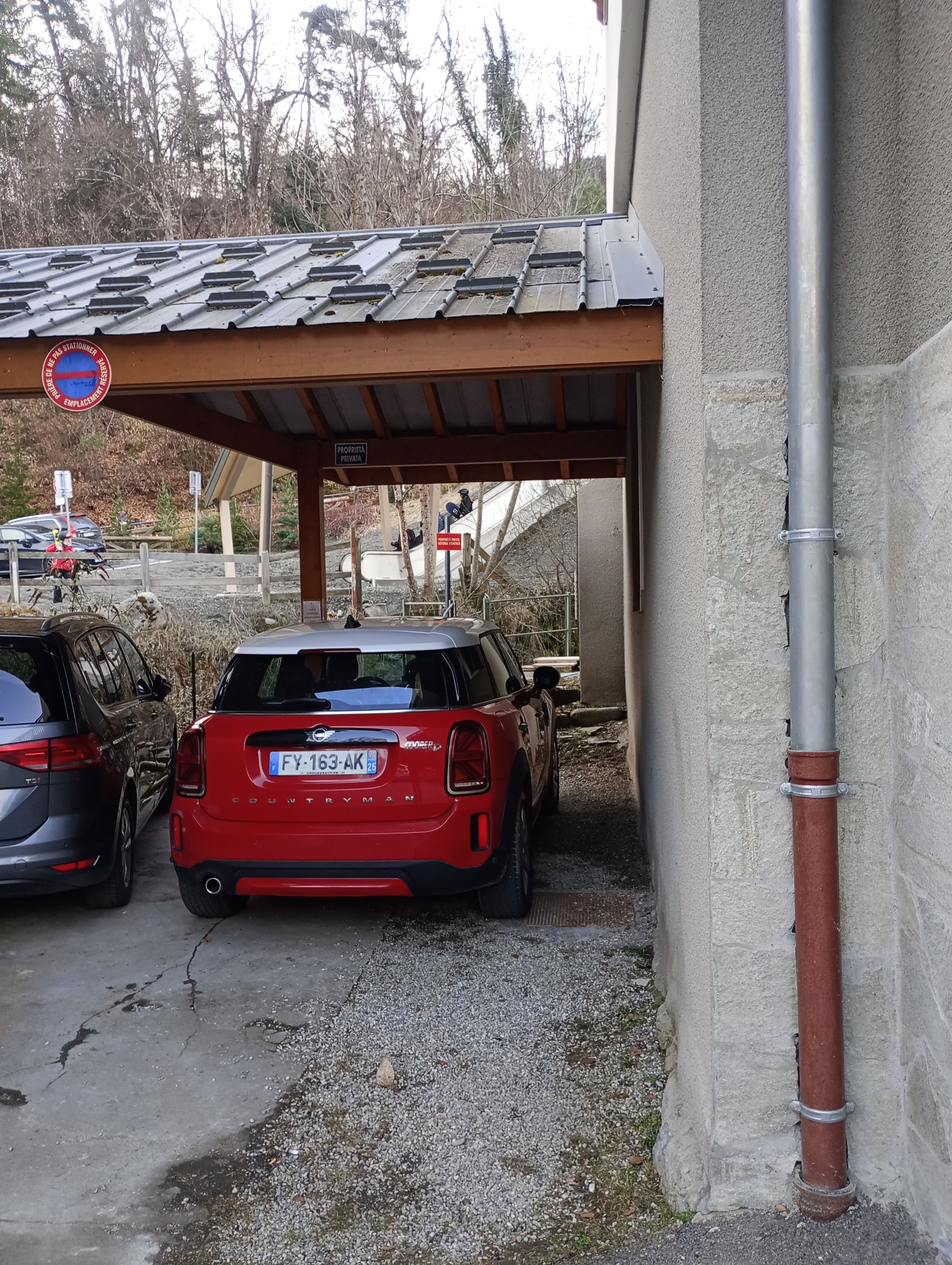 Un espace de stationnement avec deux voitures, un abri couvert et un panneau indiquant qu’il s’agit d’une propriété privée.