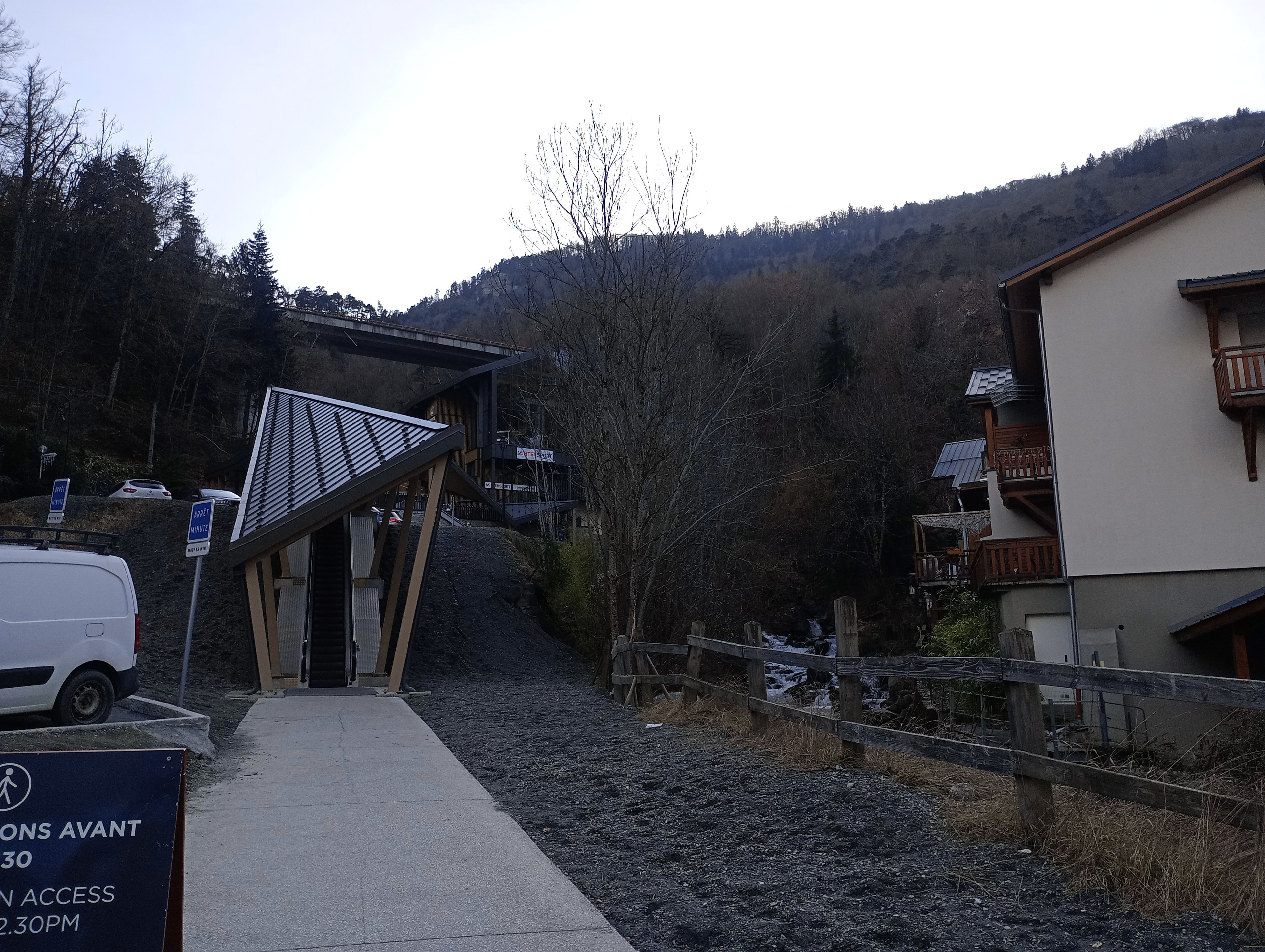 A mountain road leading to a building with a sloped roof and a sign indicating restricted access times.