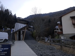 A mountain road leading to a building with a sloped roof and a sign indicating restricted access times. - Your Savoy-style apartment for skiing in the 3 Vallées, with parking at the Olympe gondola station. (Les Belleville)