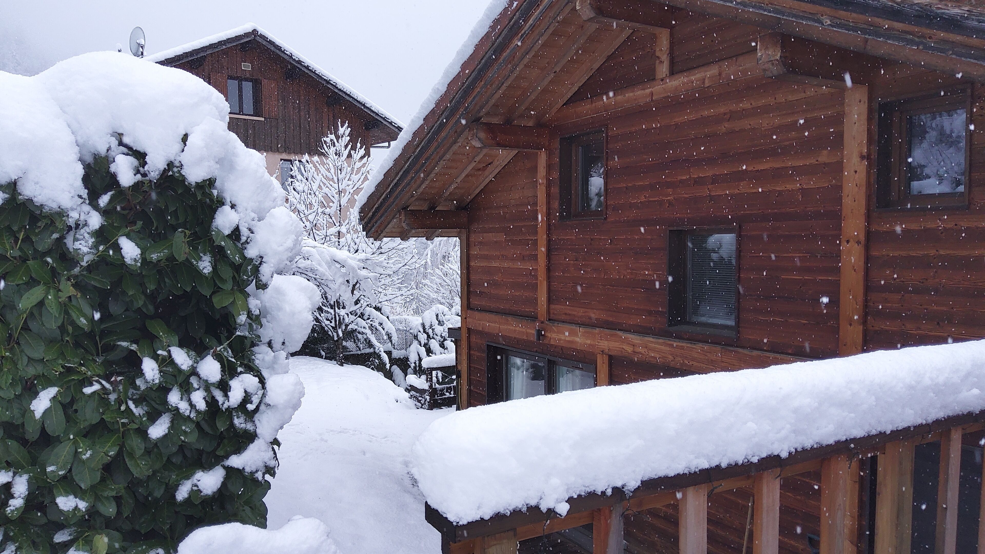 A wooden cabin with a snow-covered roof and a wooden deck.