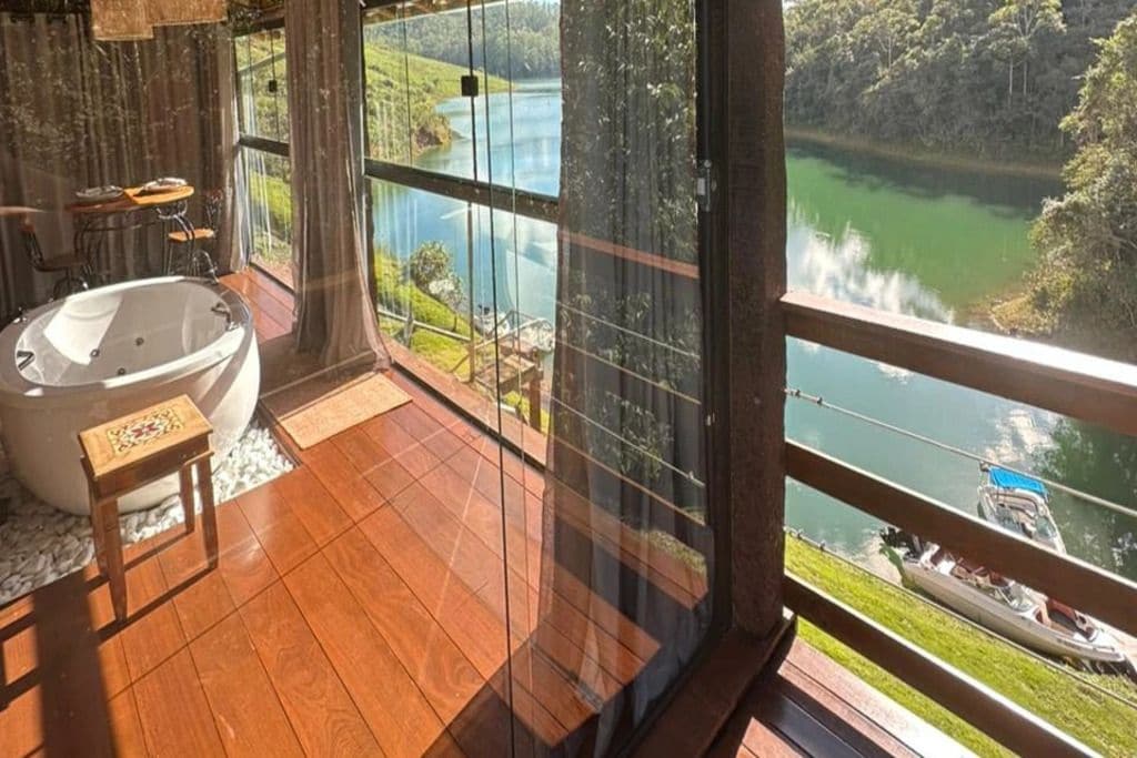Un baño con una bañera grande, suelo de madera y vistas a un río y barcos a través de amplias ventanas.