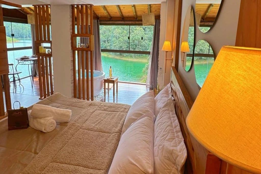 A bedroom with a large bed, a table with a bottle, and a view of a lake.