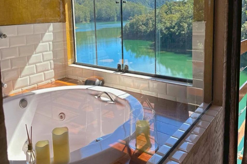Une salle de bain dotée d’une grande baignoire, d’une douche à parois de verre et offrant une vue sur un lac par le biais d’une grande fenêtre.