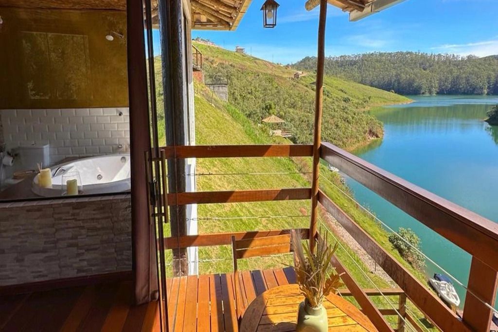 Un balcon avec vue sur un lac et des collines, une terrasse en bois et une baignoire visible à travers une porte ouverte.