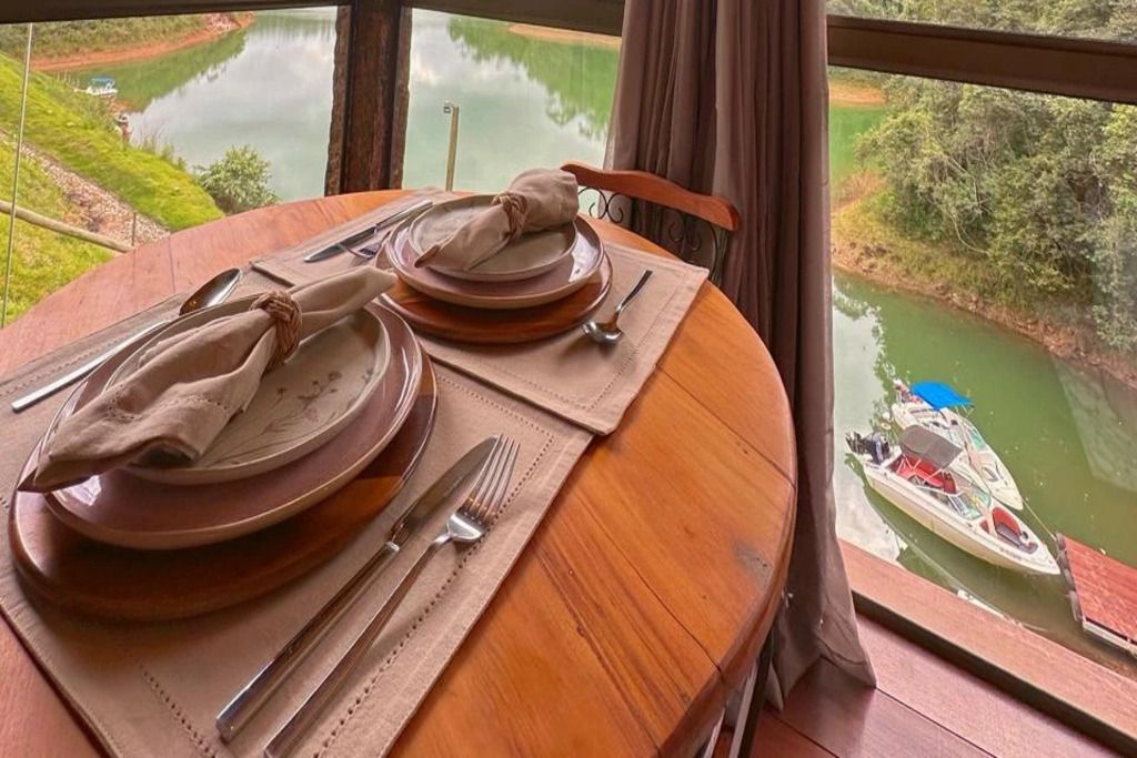 A dining table set with plates, cutlery, and napkins, overlooking a calm river and greenery.