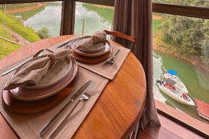 A dining table set with plates, cutlery, and napkins, overlooking a calm river and greenery.