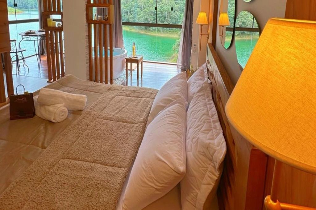 Un dormitorio con una cama grande, una lámpara de noche y vistas a una masa de agua a través de una ventana.