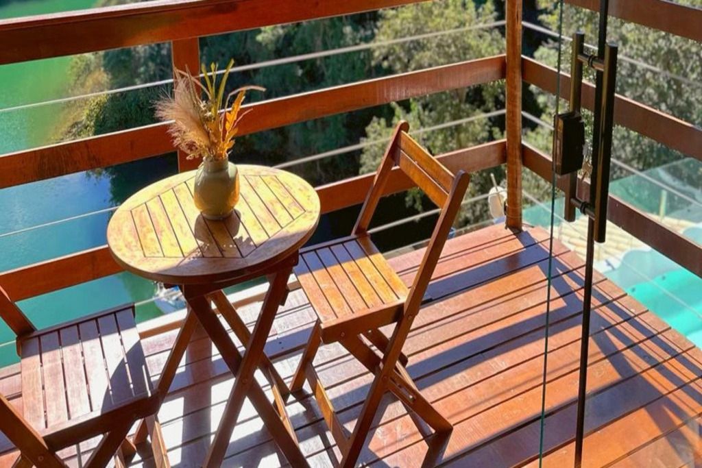 Una terraza de madera con una mesa redonda y una silla, un jarrón con plantas secas, y vistas a un cuerpo de agua.