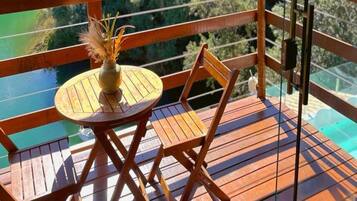 Una terraza de madera con una mesa redonda y una silla, un jarrón con plantas secas, y vistas a un cuerpo de agua.