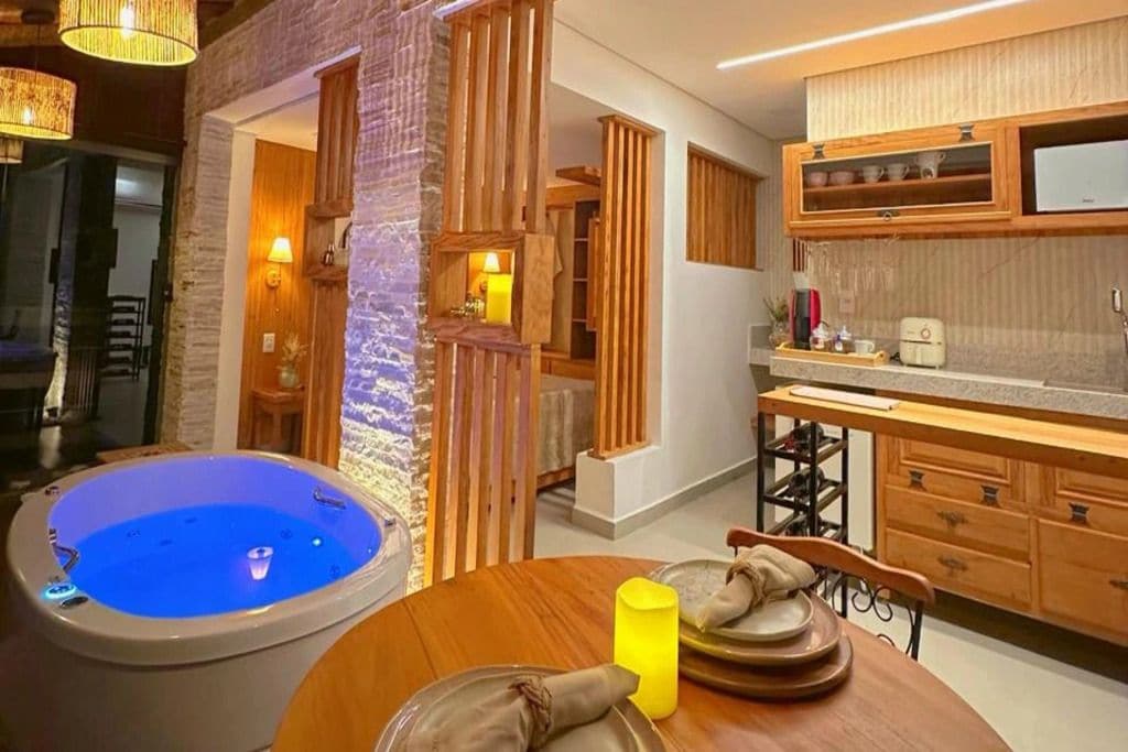 A room with a hot tub, wooden cabinets, a dining table with plates, and a yellow candle.
