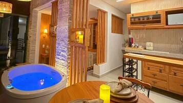 A room with a hot tub, wooden cabinets, a dining table with plates, and a yellow candle.