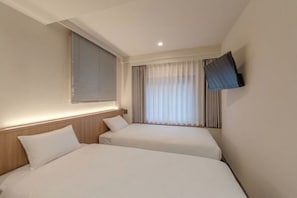 Habitación de hotel con dos camas, un televisor montado en la pared y una ventana con cortinas.
