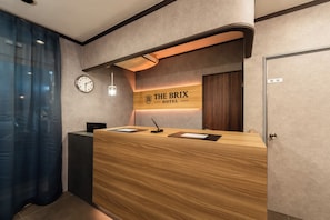 Un mostrador de recepción con un reloj, un cartel que dice 'THE BRIX HOTEL' y una puerta a la derecha.