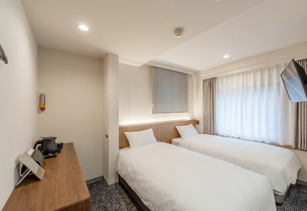 Habitación de hotel con dos camas, un escritorio con hervidor, televisión de pantalla plana y ventana con cortinas.