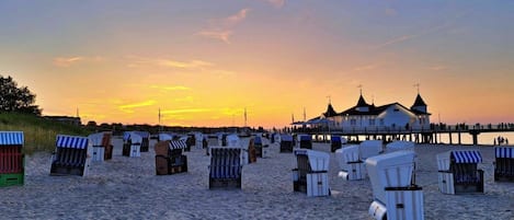 A beach with rows of beach chairs and a pier with a building at the end.