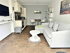 A modern living room with a grey sofa, a white coffee table, and a kitchen area with a microwave and stove. - Holiday Apartment Altenberg 02 (Heringsdorf)