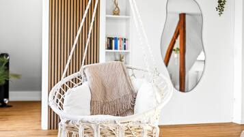 A macrame hanging chair with a cushion and a blanket, a wooden floor, a bookshelf, and a mirror on the wall.