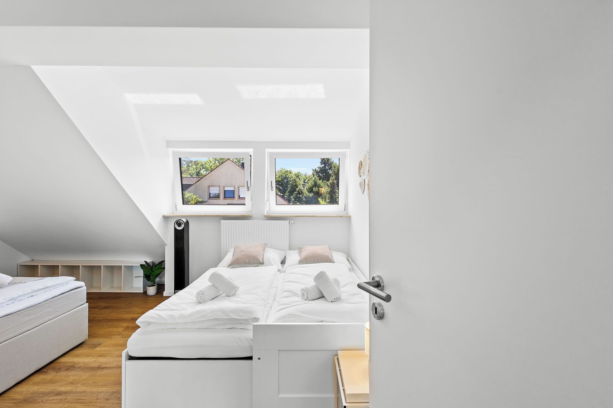A modern bedroom with a loft-style ceiling, a bed with white bedding, and two windows offering views of the outside.