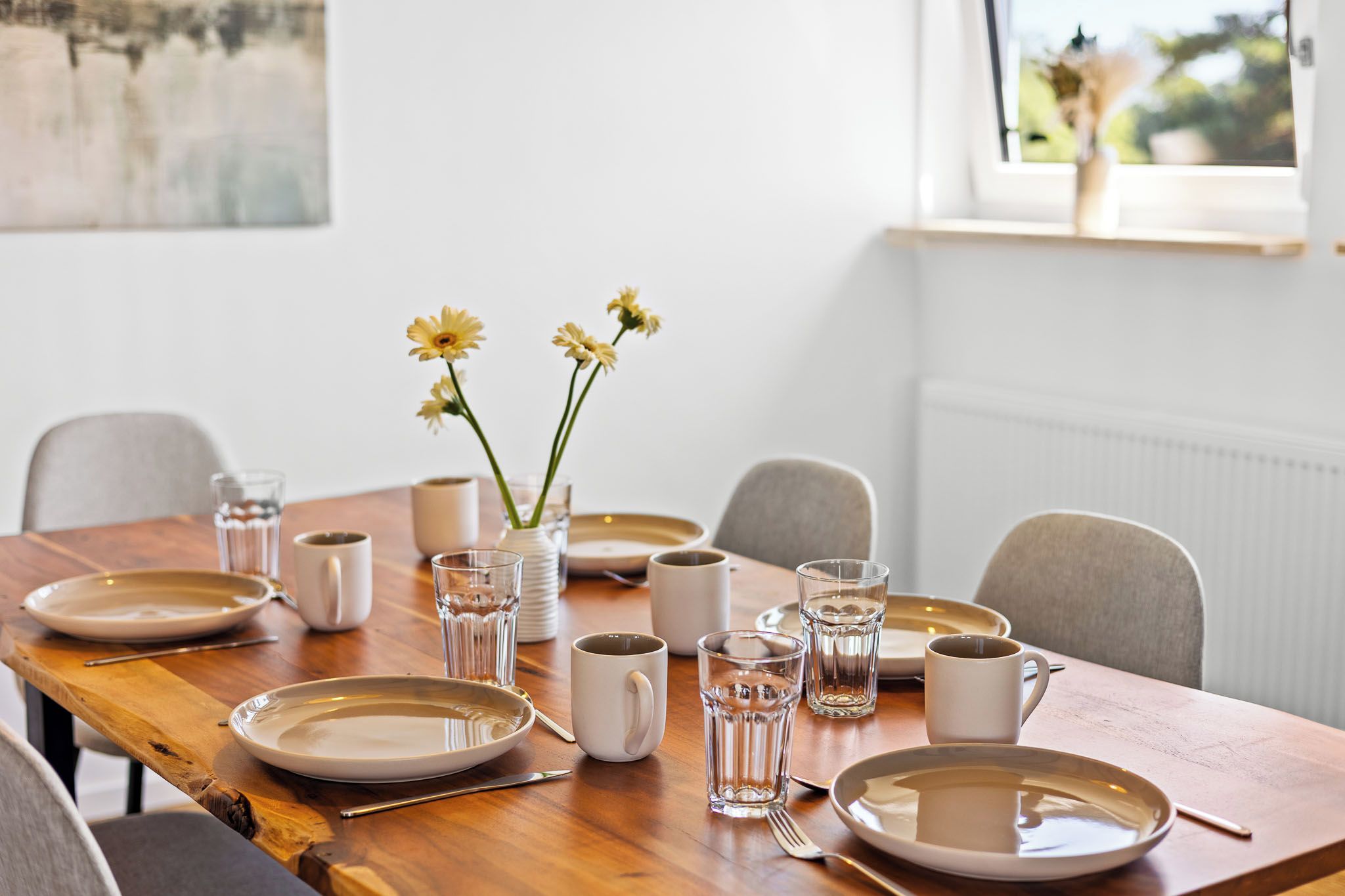 A dining table set with plates, glasses, and a vase with flowers.
