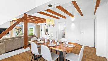 Un espace repas moderne avec une table en bois, des chaises grises et une vue sur l’extérieur.