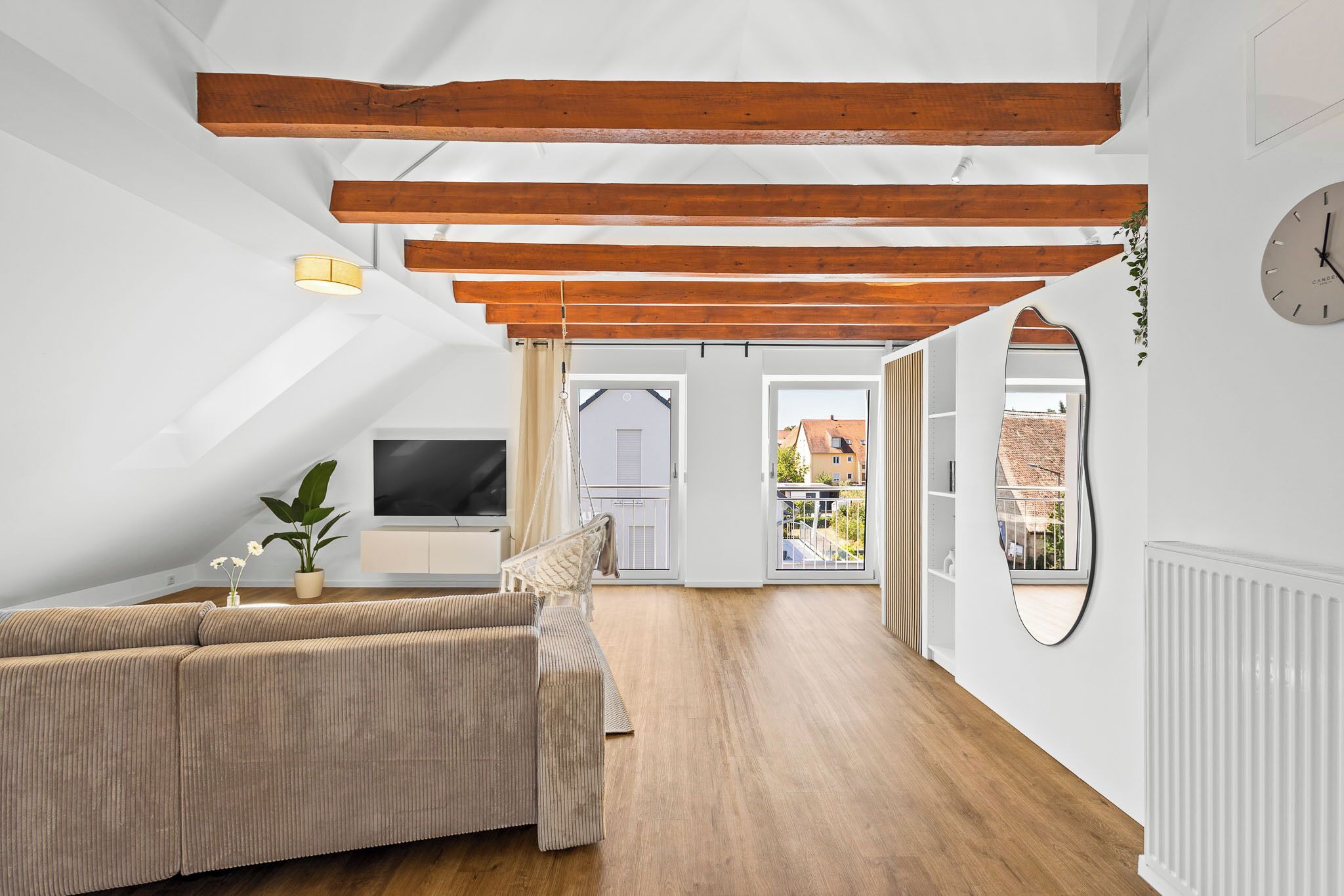 A modern loft with exposed wooden beams, a large window, and a cozy seating area.