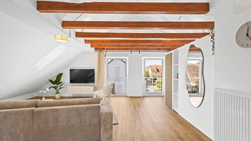 A modern loft with exposed wooden beams, a large window, and a cozy seating area.