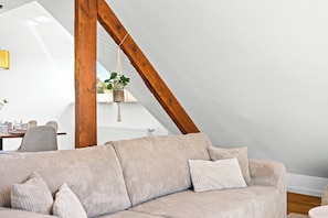 A loft-style room with a high ceiling, exposed wooden beams, a beige sofa, and a hanging plant.
