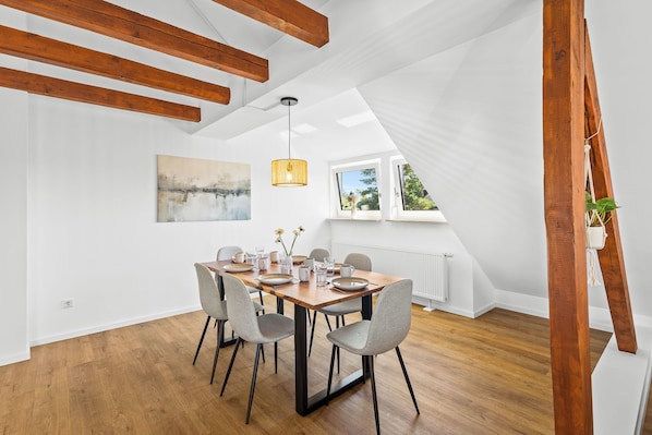 A dining area with a wooden table, grey chairs, and a painting on the wall.