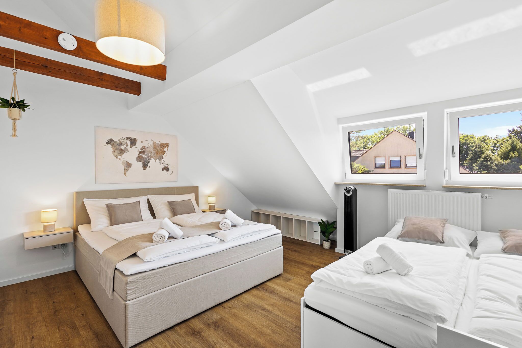 Une chambre à coucher moderne avec un grand lit, une carte du monde accrochée au mur et une vue sur une maison par la fenêtre.