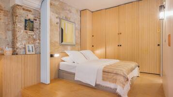 Une chambre à coucher avec un lit en bois, une table de chevet, une lampe fixée au mur et une armoire en bois.