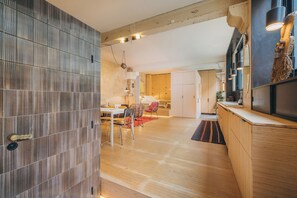 A modern kitchen with wooden cabinets, a dining area with a table and chairs, and a hallway leading to a bedroom.